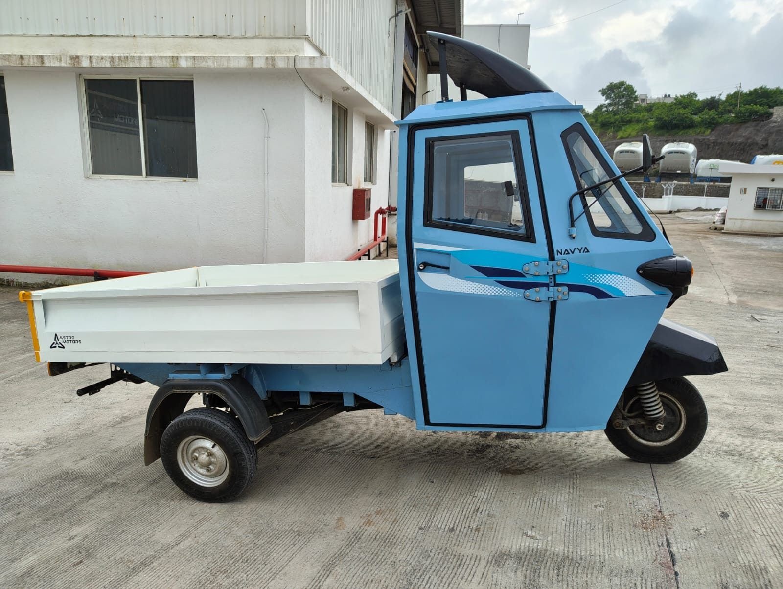 Side view of a painted blue Navya with white flatbed outside the factory