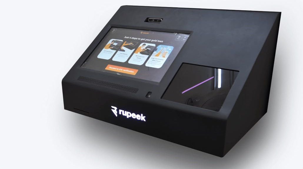 The Rupeek Gold Teller Machine — a black desk-height kiosk with an angled touchscreen and a gold tray